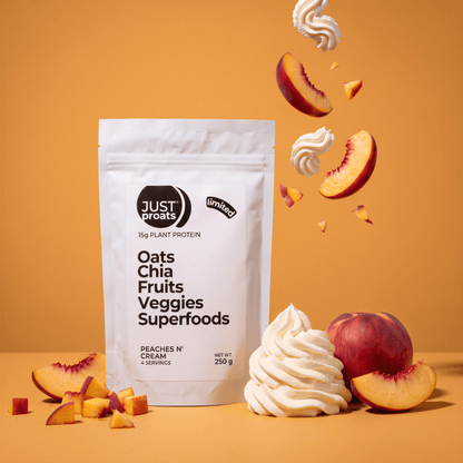A stand-up pouch of Just Proats plant protein powder in Peaches, n' Cream flavor, styled with peach slices, whipped cream swirls, and whole peaches on a warm orange background.