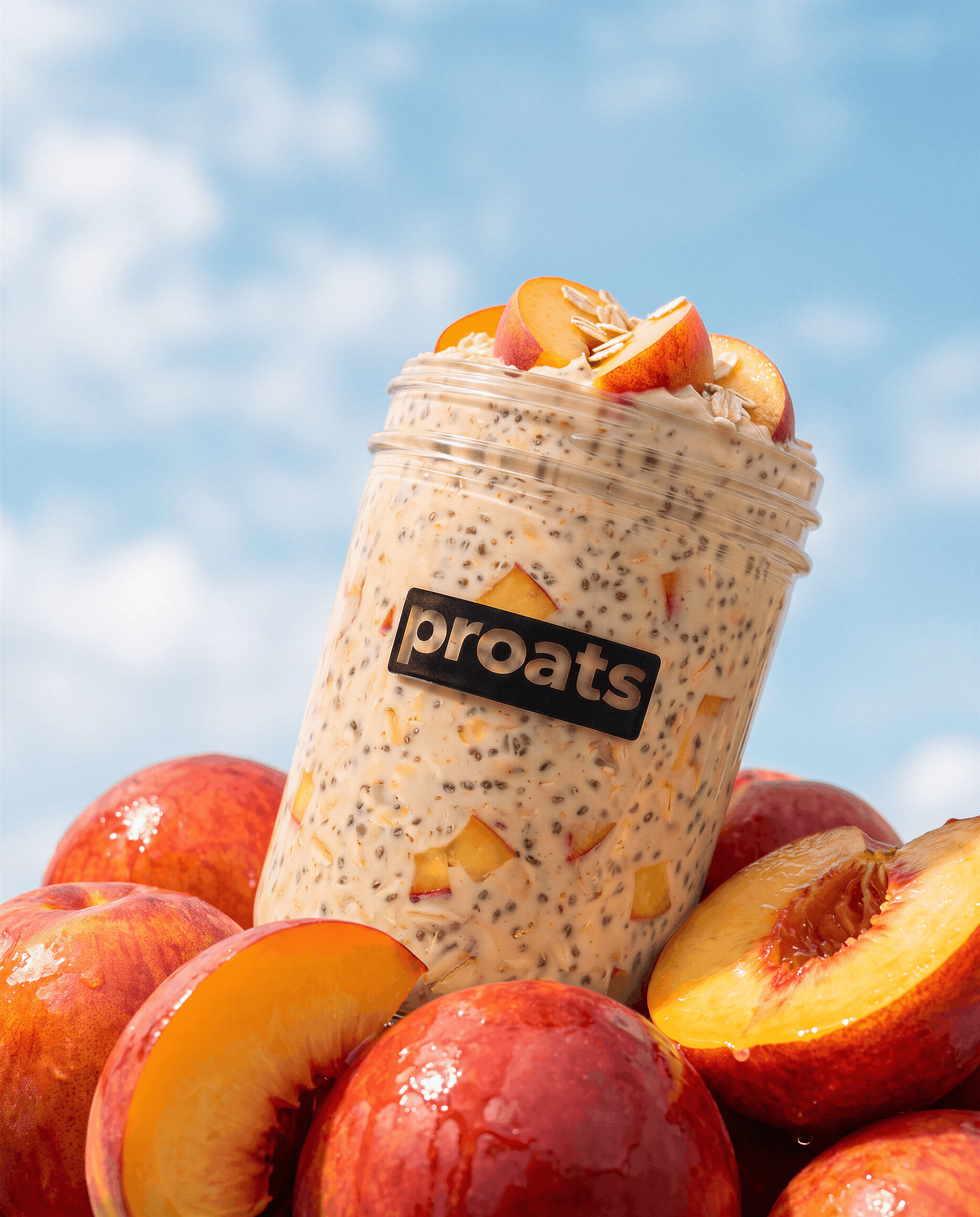 A Proats jar, topped with peach slices, surrounded by fresh whole and sliced peaches against a bright blue sky background.