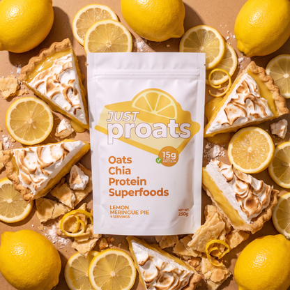 A white stand-up pouch of Just Proats Oats Chia Protein Superfoods, Lemon Meringue Pie flavor, styled in a flat-lay arrangement with lemon slices, whole lemons, and lemon meringue pie tart slices on a tan background.